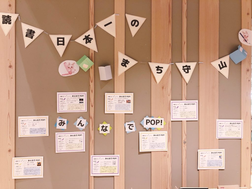 木製の壁に「読書日本一のまち守山」「みんなでPOP!」の文字と、複数の本の紹介POPを飾った展示。